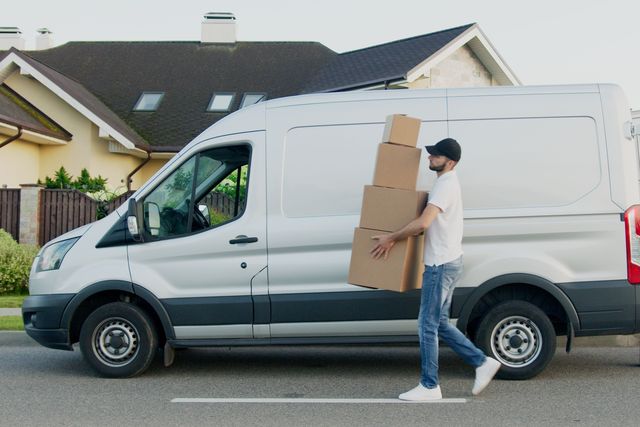 Een man draagt verhuisdozen langs een witte bestelwagen